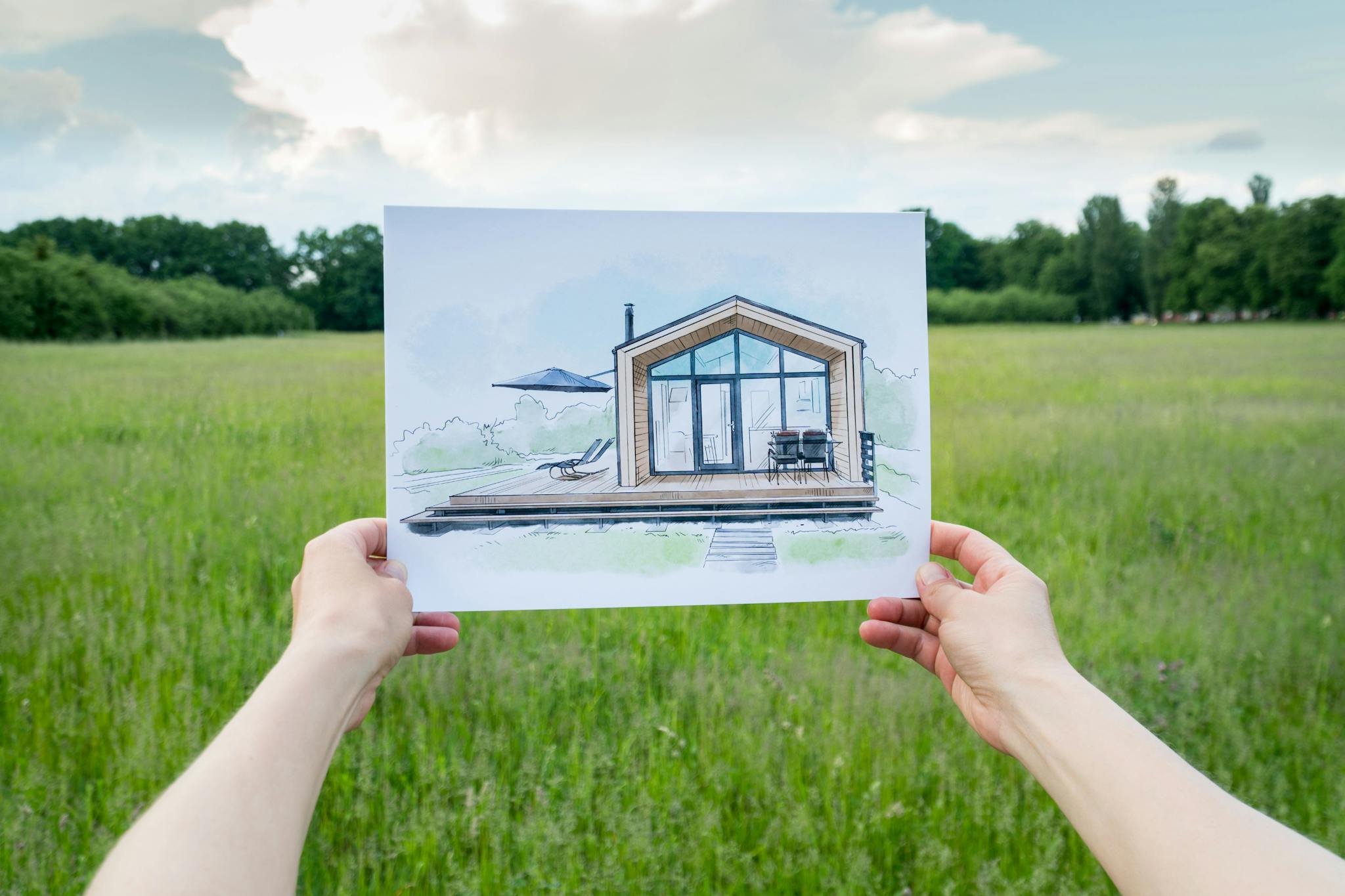 Person in a field holding a drawing of a house 
